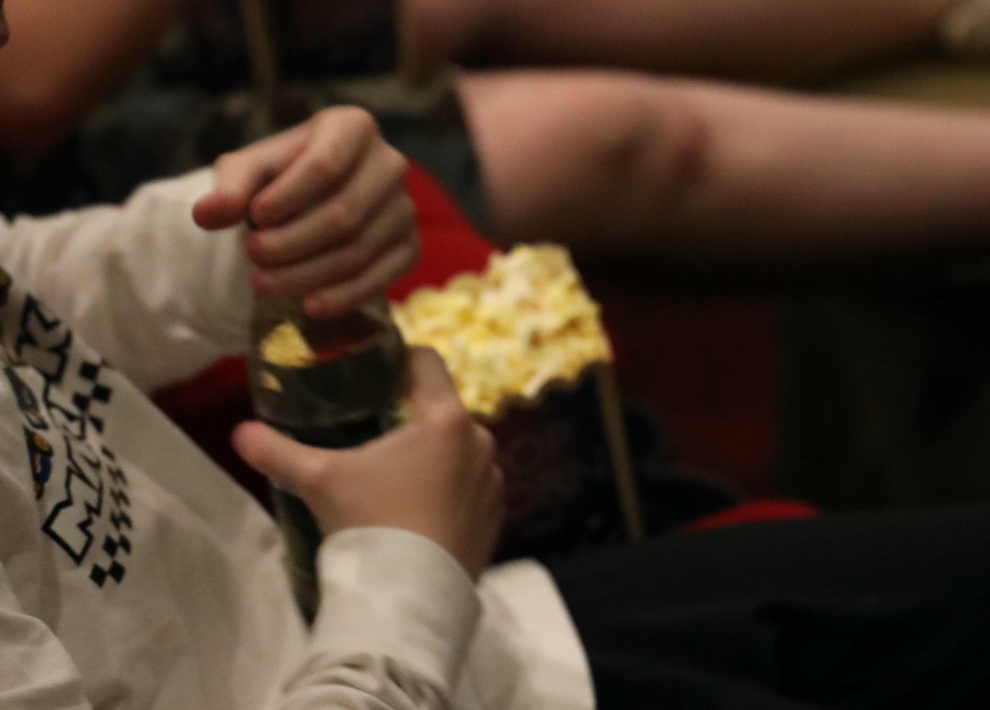 Barnhänder som öppnar en läskflaska och popcorn i bakgrunden