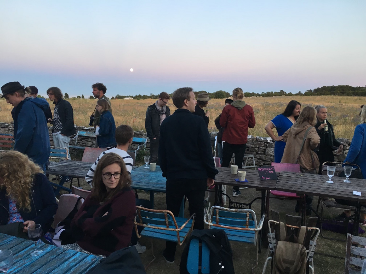 Bord, stolar, människor som sitter och står efter en god middag ute i kvällsljuset på Gotland.