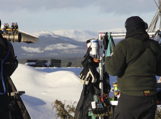 Två filmarbetare i vinterlandskap, en håller i en kamera.