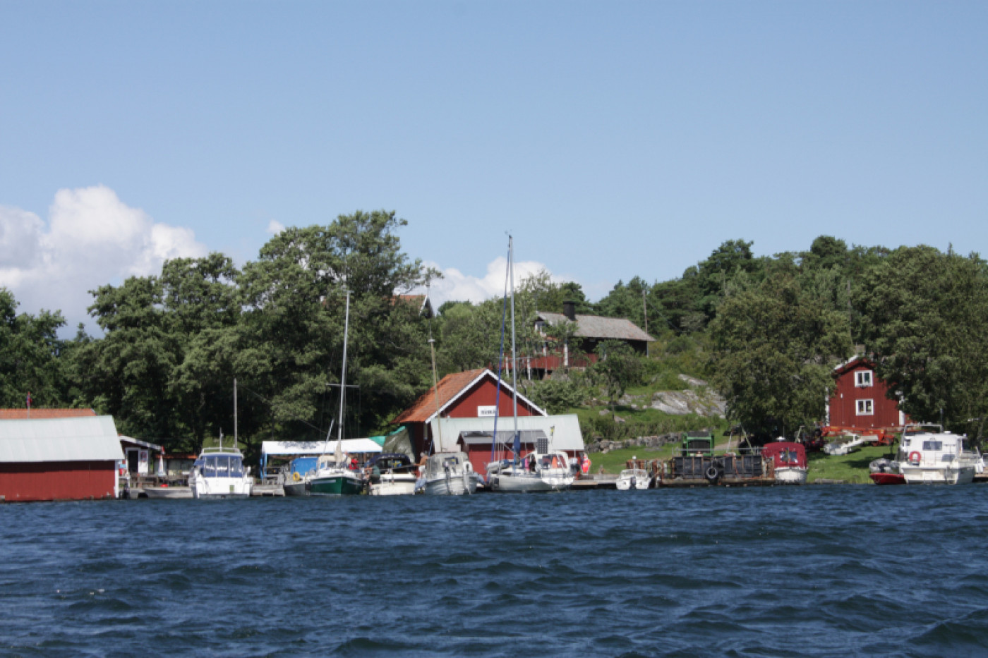 Liten hamn med båtar och röda stugor i Håsk Skärgård.