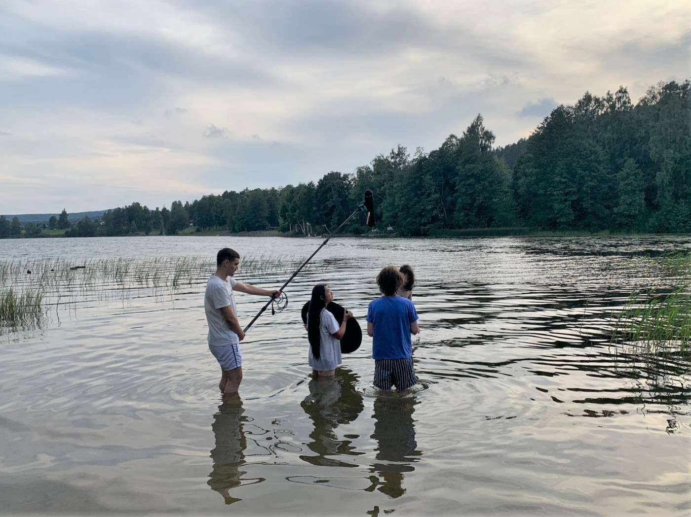 Tre ungdomar står i en sjö med filmkamera och mikrofon. De spelar in en filmscen. 