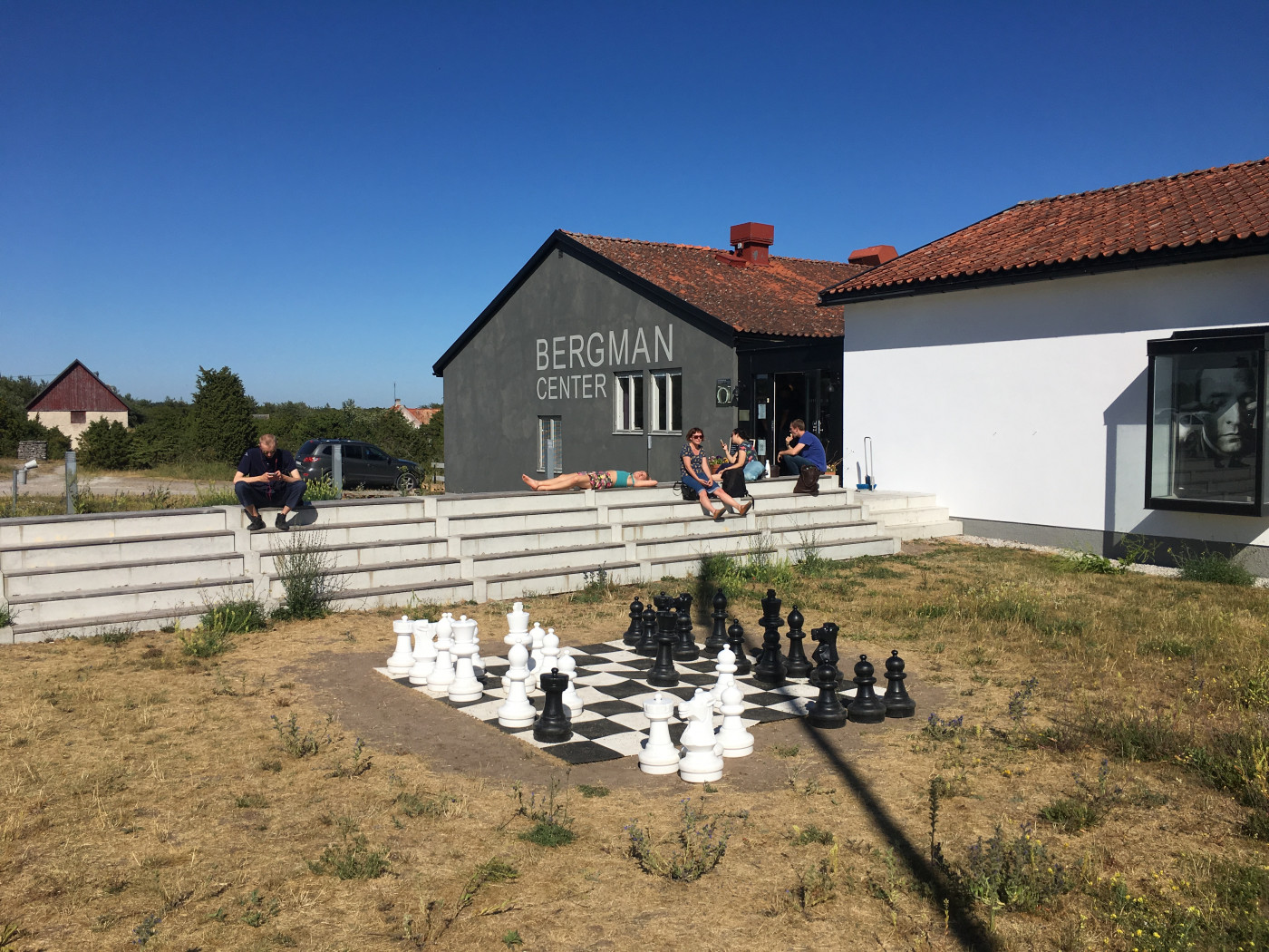 Foto från Bergmancenter på Fårö. Ungdomar sitter i solen och vilar. Ett stort schackspel är i förgrunden. 
